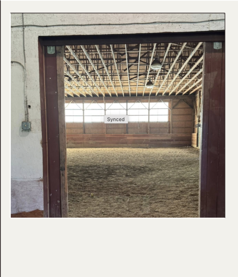 looking into an indoor riding rink through a wide brown barn door